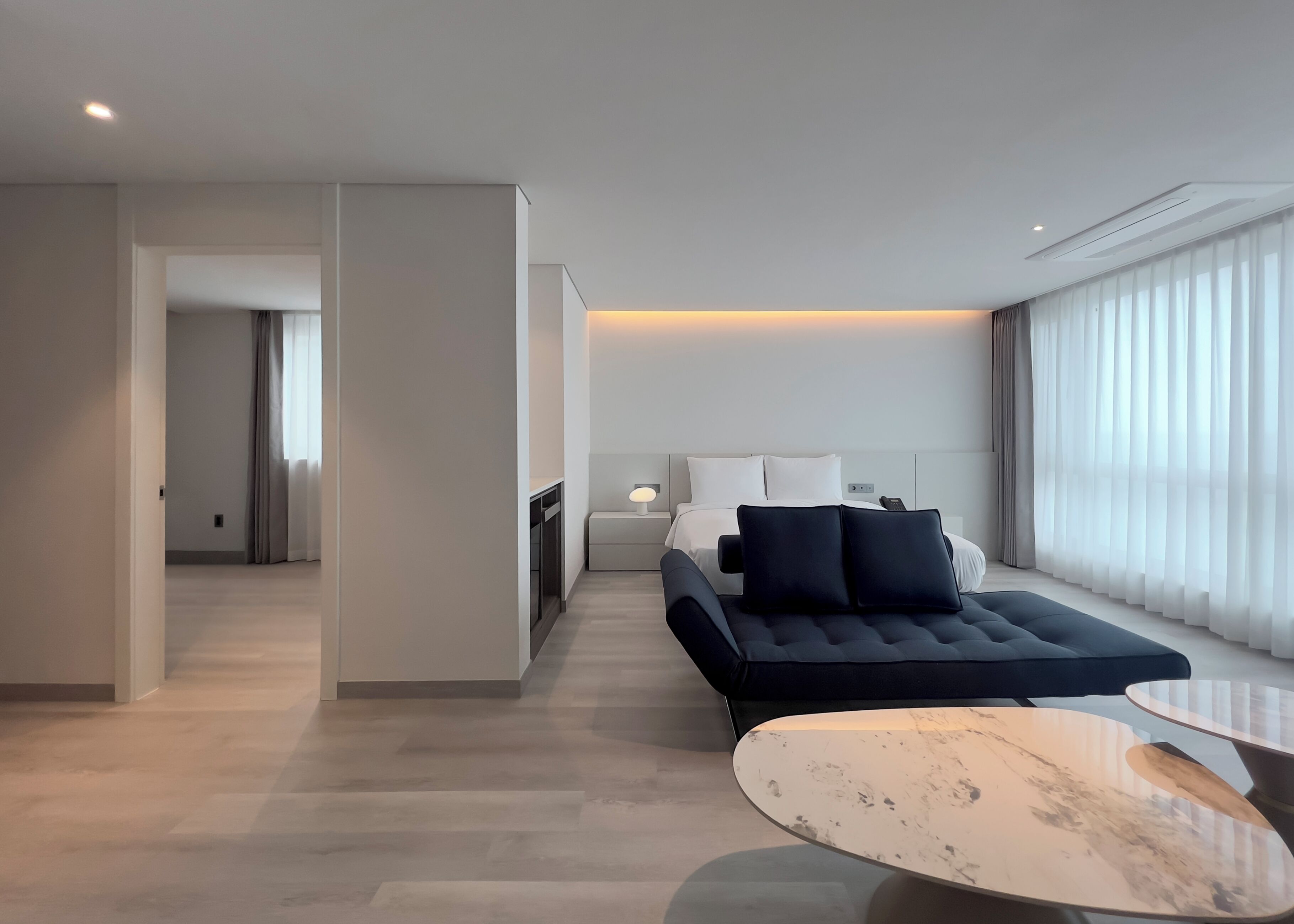 Ein modernes Hotelzimmer mit Bett, Sofa, einem kleinen Tisch und Blick auf die Stadt durch große Fenster.