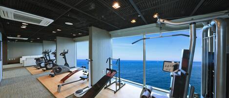 Uma academia com equipamentos de exercícios, amplas janelas e vista para o oceano.