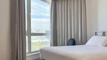 A hotel room with a large window, a bed, a chair, and a control panel on the wall.