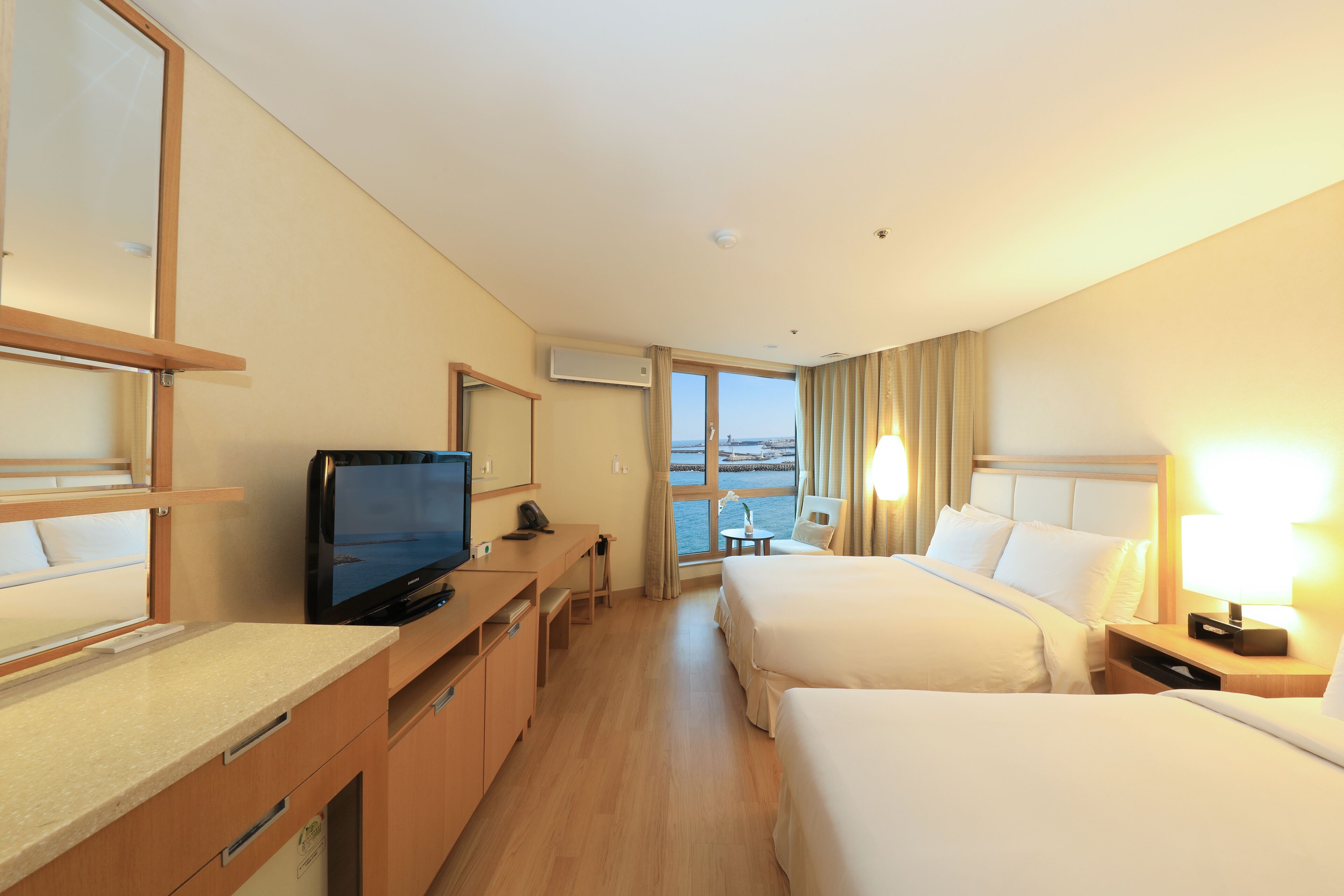 Une chambre d’hôtel avec deux lits, un bureau avec une télévision et une vue sur la mer.