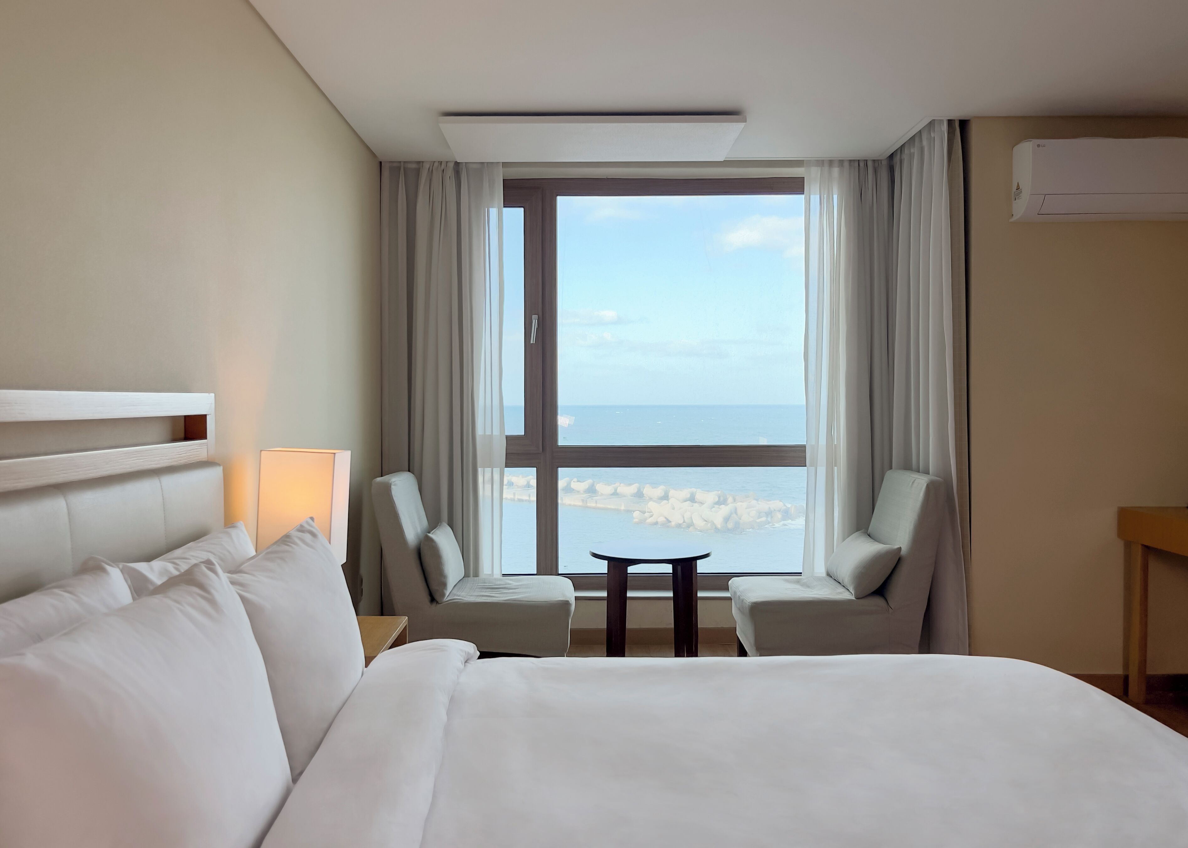 A hotel room with a large bed, two armchairs, a small table, and a view of the sea through a large window.