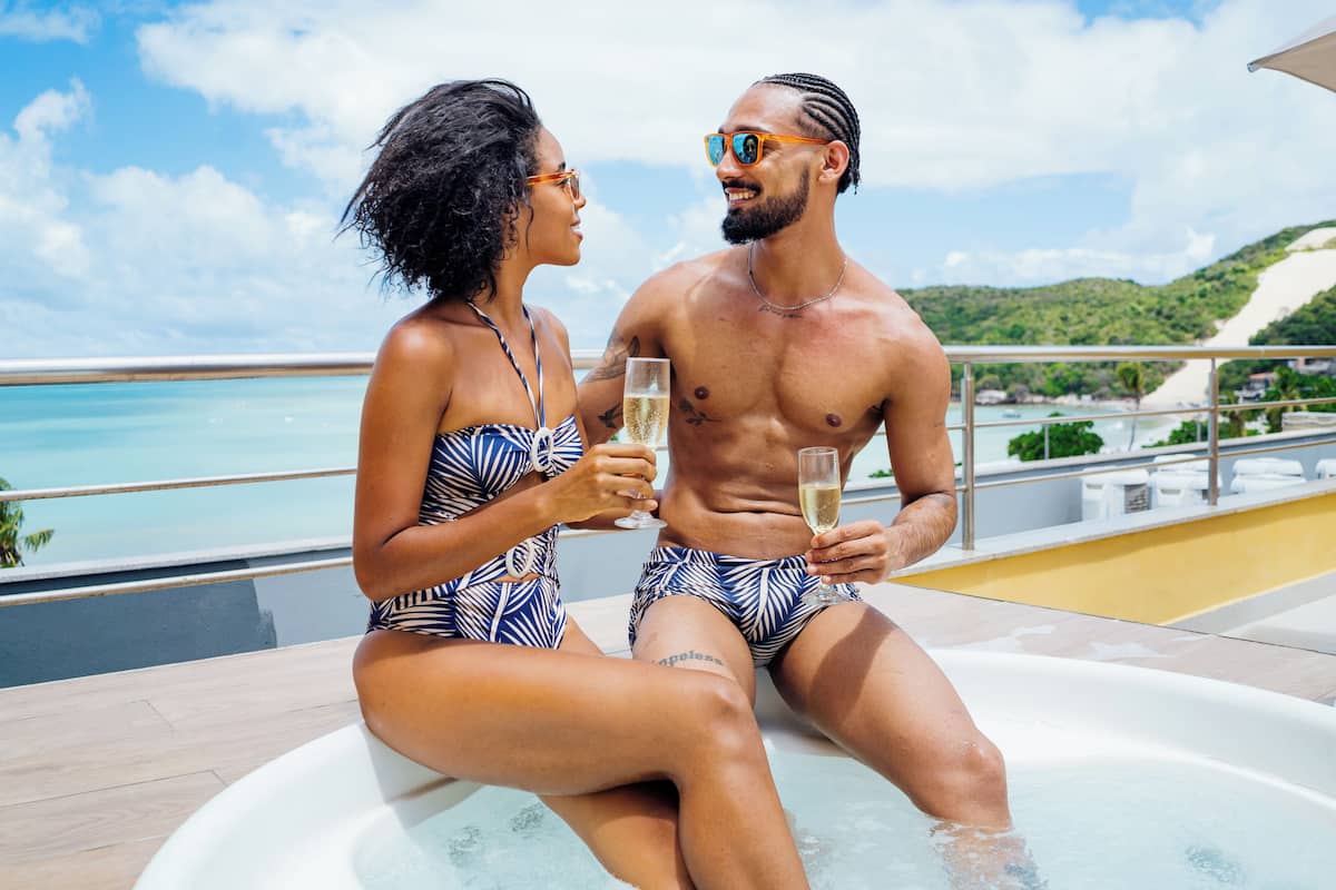 A couple sitting by a hot tub with a scenic view of the ocean and hills.