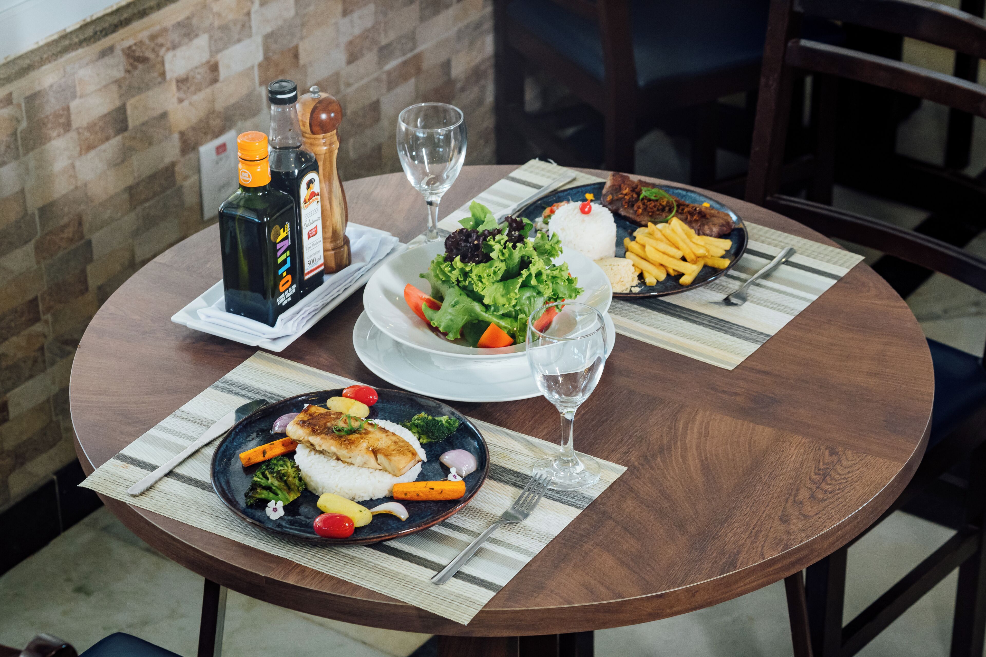 Una mesa redonda con platos de comida, vasos de agua y botellas de aceite de oliva.