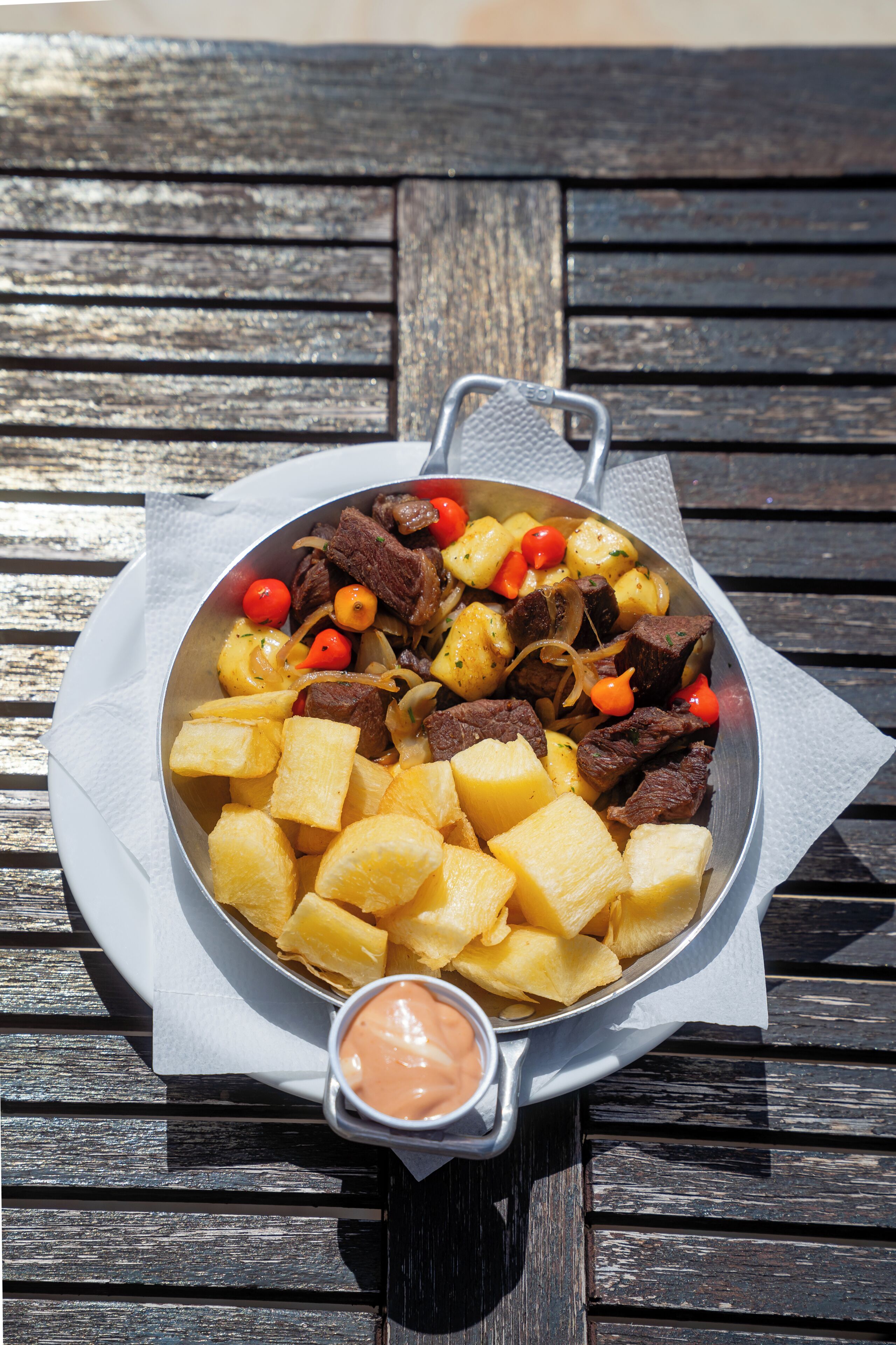 Un plato de carne, papas y tomates sobre una mesa de madera.