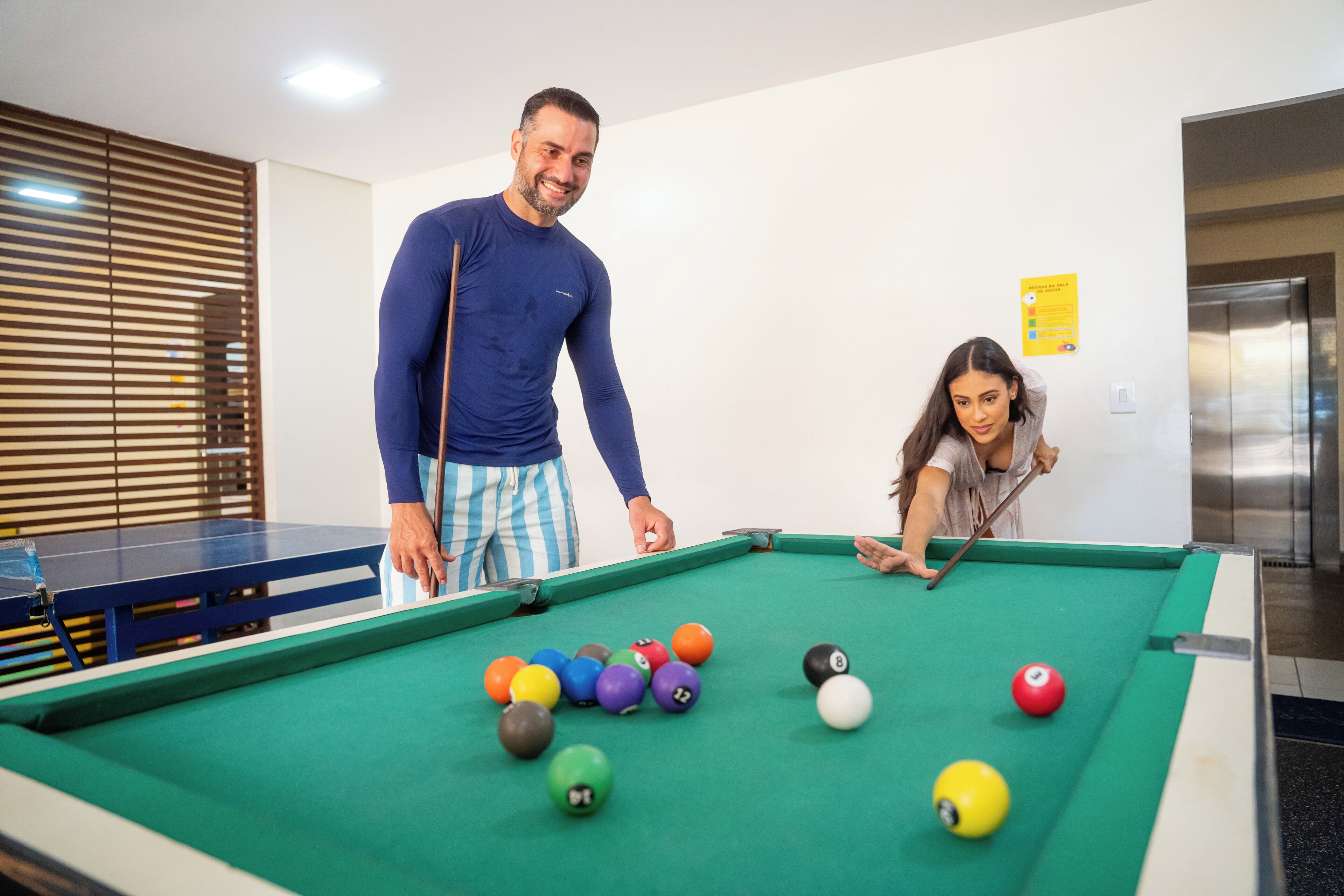 A pool table with balls, a person standing, and another leaning over the table.