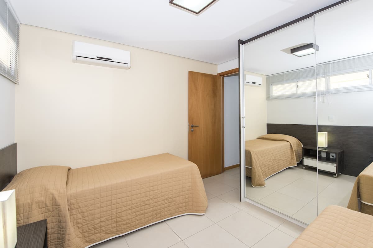 A hotel room with two beds, a large mirror, a wardrobe, and a ceiling fan.