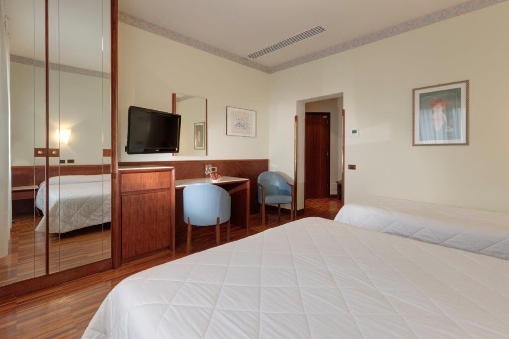 Habitación de hotel con cama, escritorio con silla, televisor y puerta que da a otra habitación.