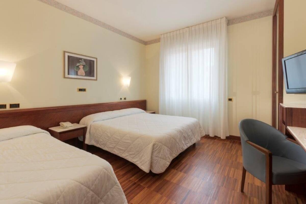 Hotellihuone, jossa on kaksi sänkyä, työpöytä, tuoli, televisio ja taulu seinällä.