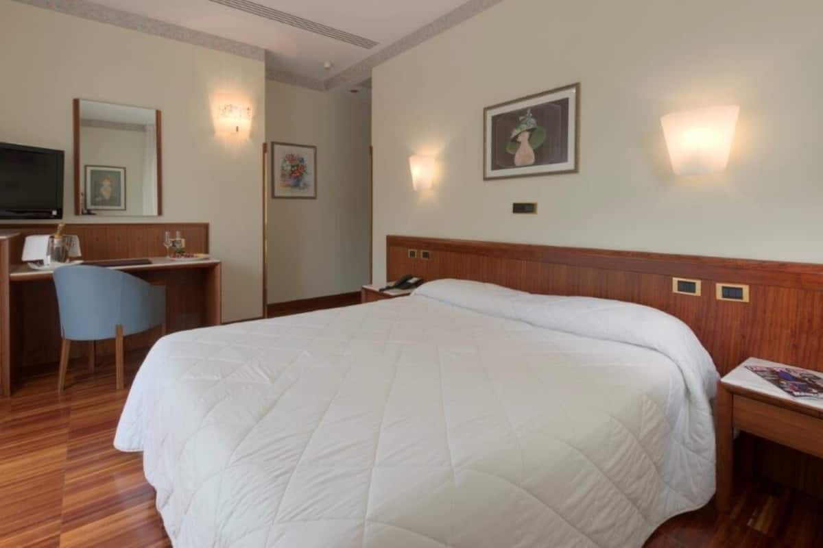 Hotellihuone, jossa on suuri sänky, työpöytä tuolilla, televisio ja seinään kiinnitetyt valaisimet.