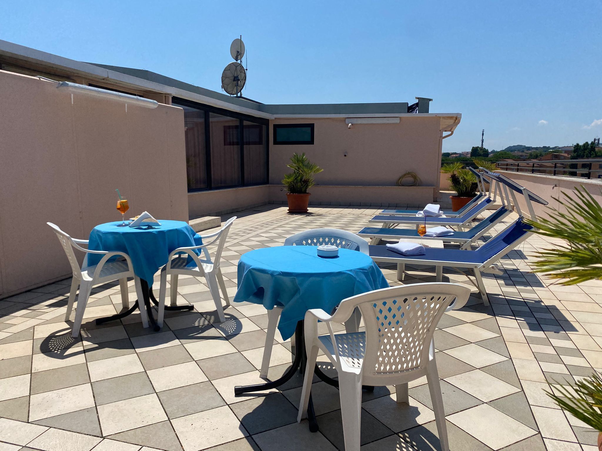 Eine Dachterrasse mit blauen Tischdecken, weißen Stühlen und Liegestühlen.