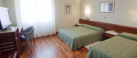 A hotel room with two single beds, a desk with a computer, a chair, and a window with curtains.