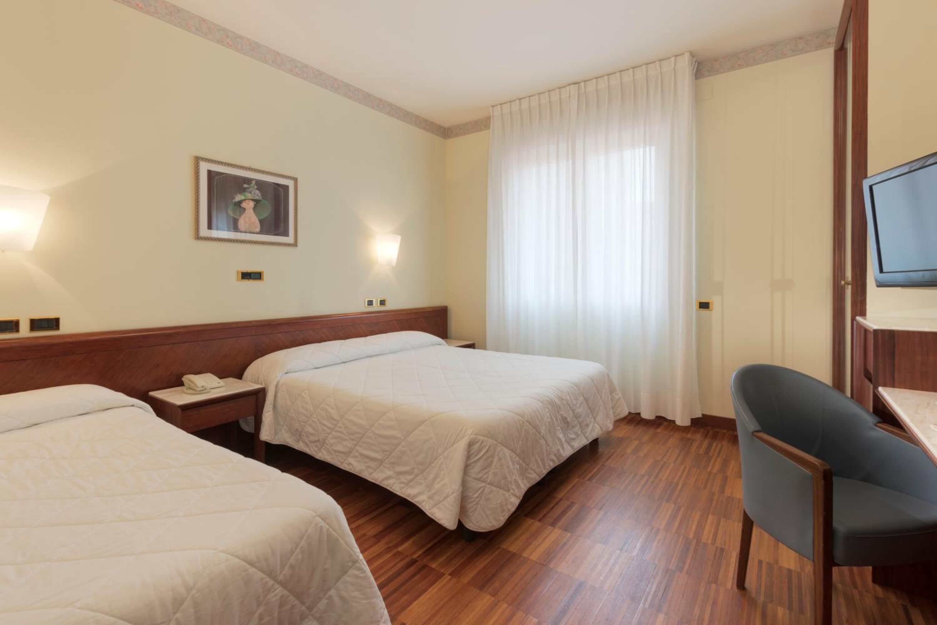 A hotel room with two beds, a desk, a chair, a television, and a painting on the wall.