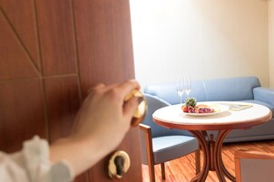 A person unlocking a door to a room with a round wooden table, a blue sofa, and a small potted plant.