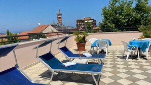 A rooftop terrace with blue lounge chairs, a table with a blue tablecloth, and a potted plant. - Palace Hotel (Civitanova Marche)