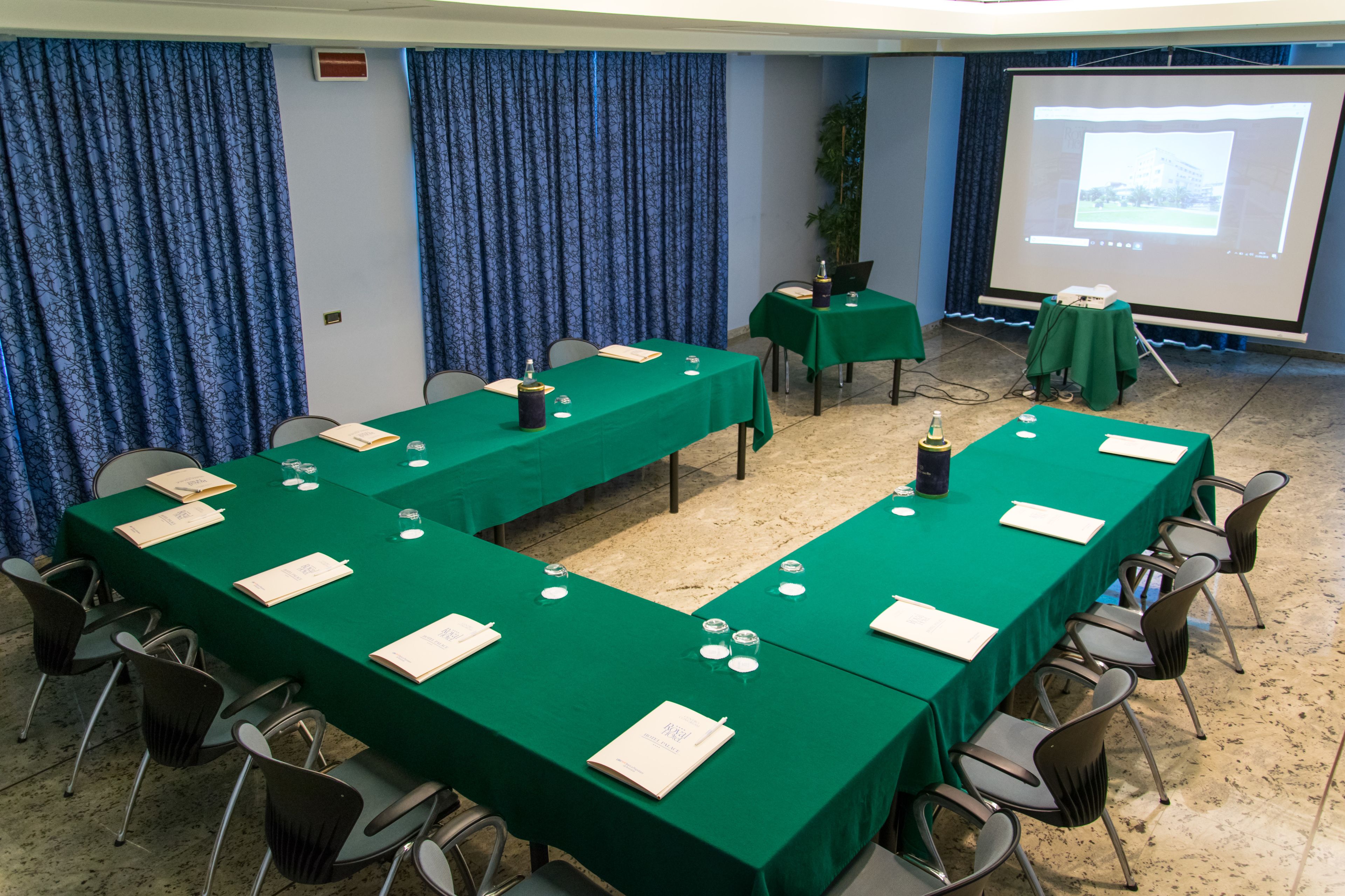 A conference room with long tables, chairs, a projector screen, and a presentation screen.