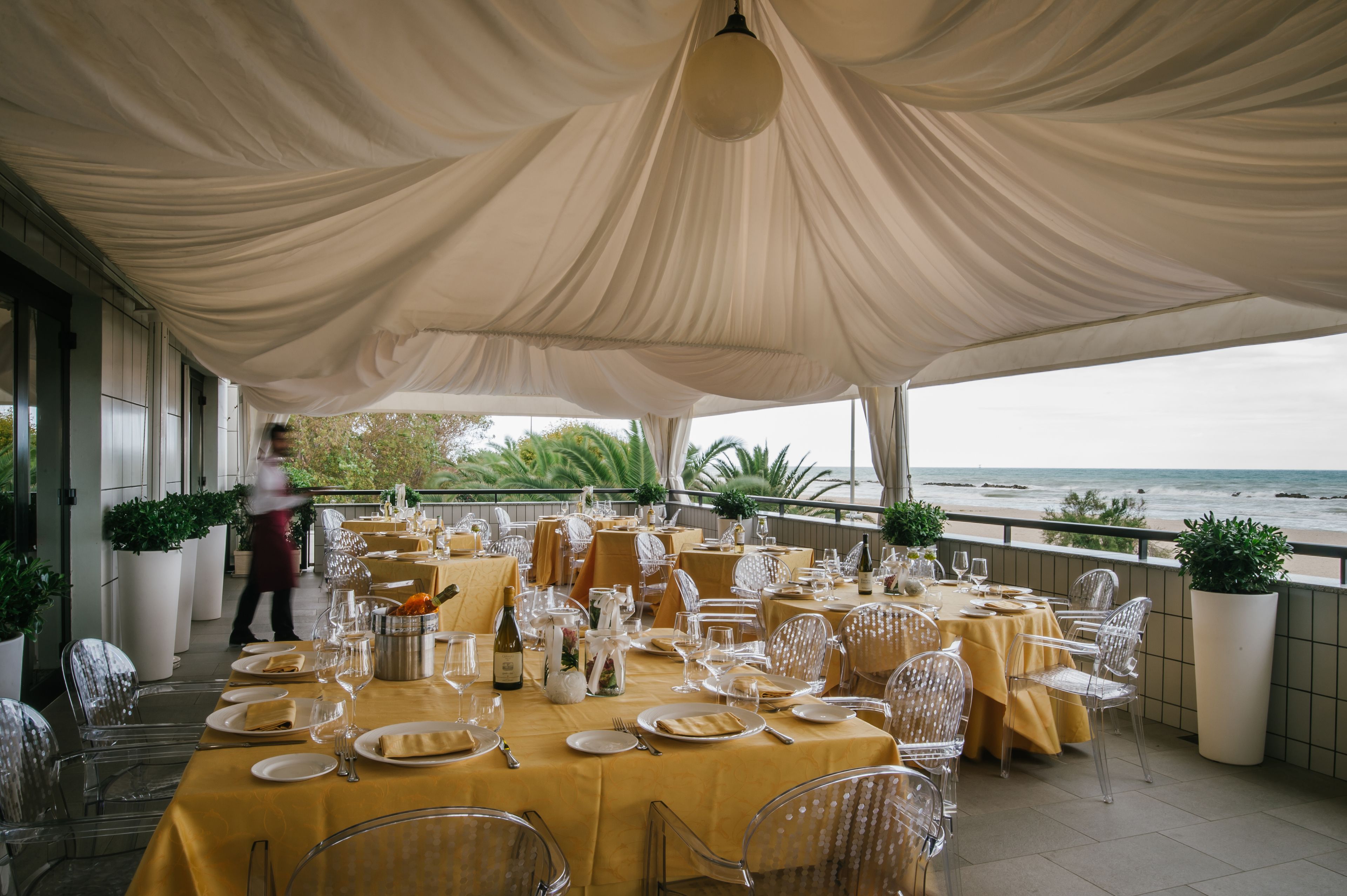 An outdoor dining area with tables set for a meal, overlooking the sea.