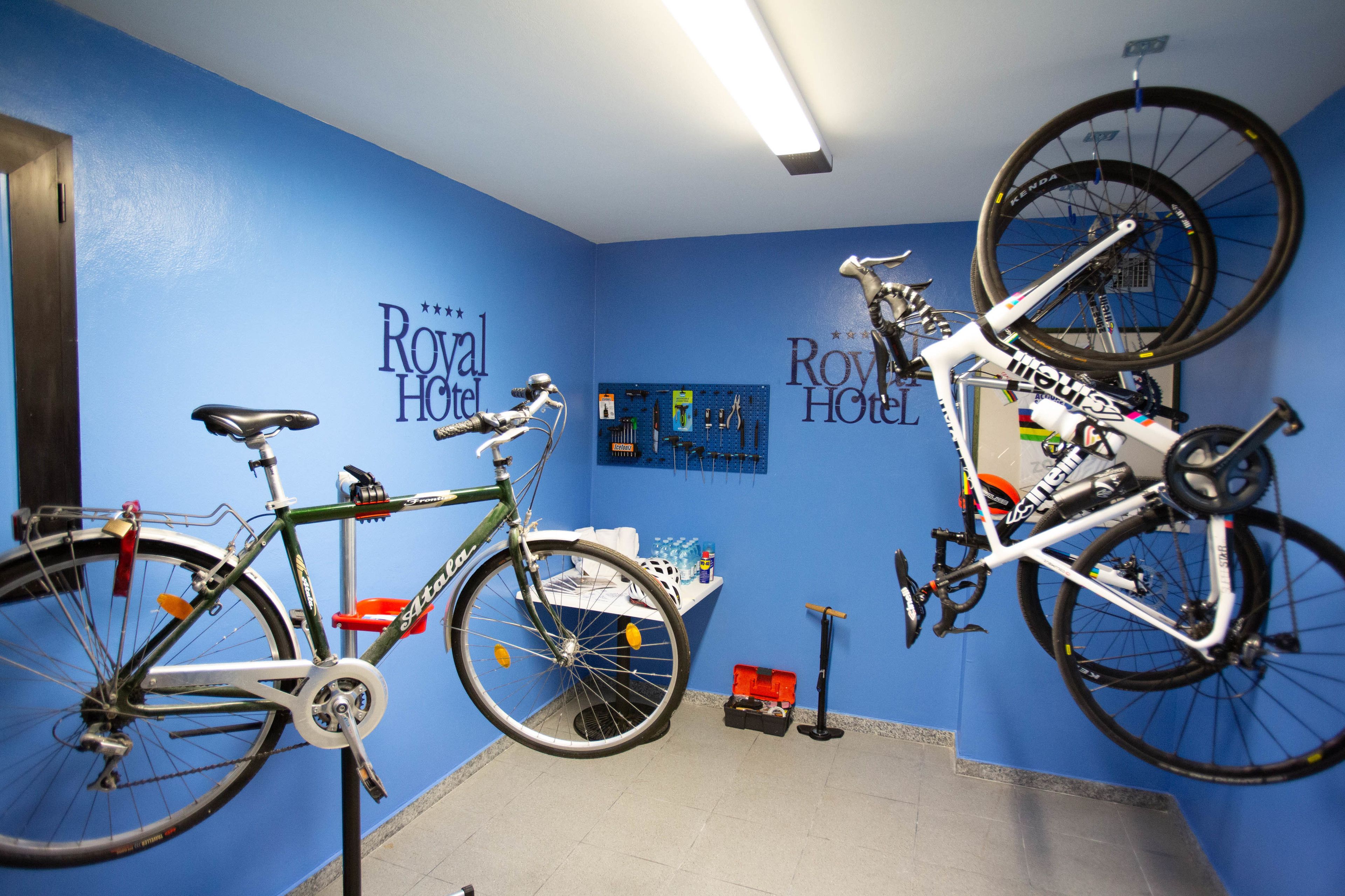 Una habitación con dos bicicletas colgadas en la pared, un soporte para bicicletas y un estante para herramientas también en la pared.