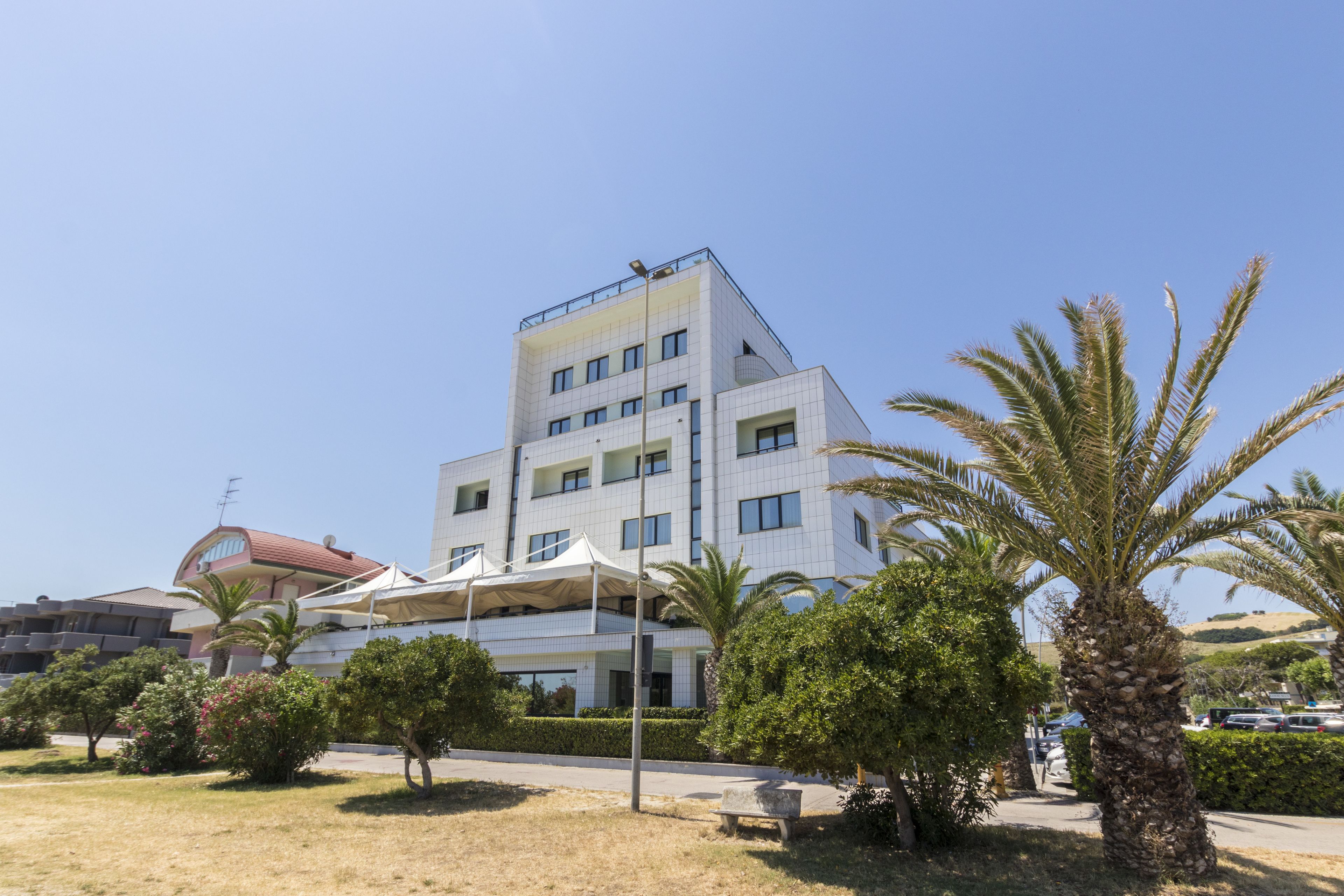 A multi-story building with a flat roof, surrounded by greenery and a clear sky.