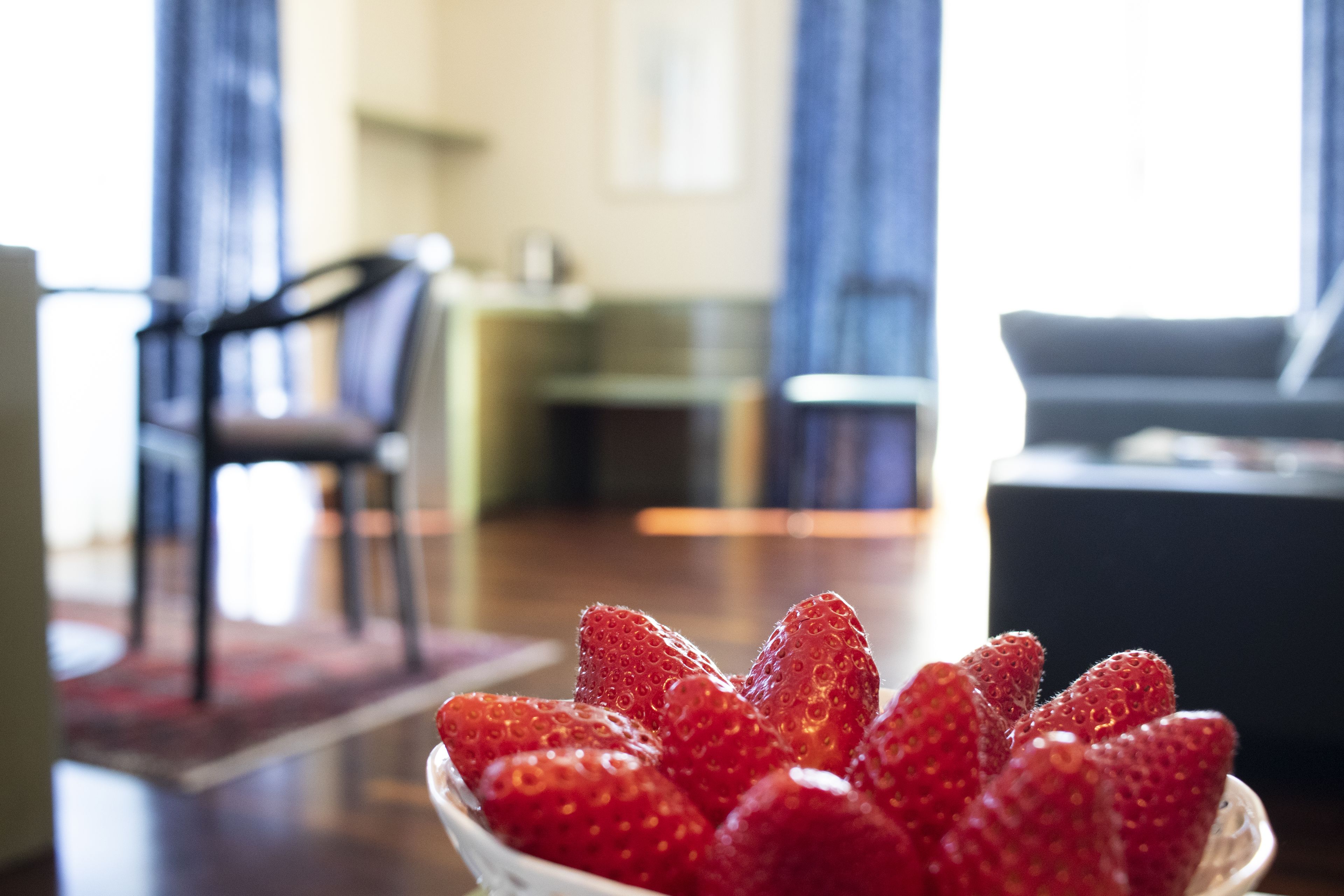 A bowl of strawberries on a table in a living room with a chair and a sofa in the background.