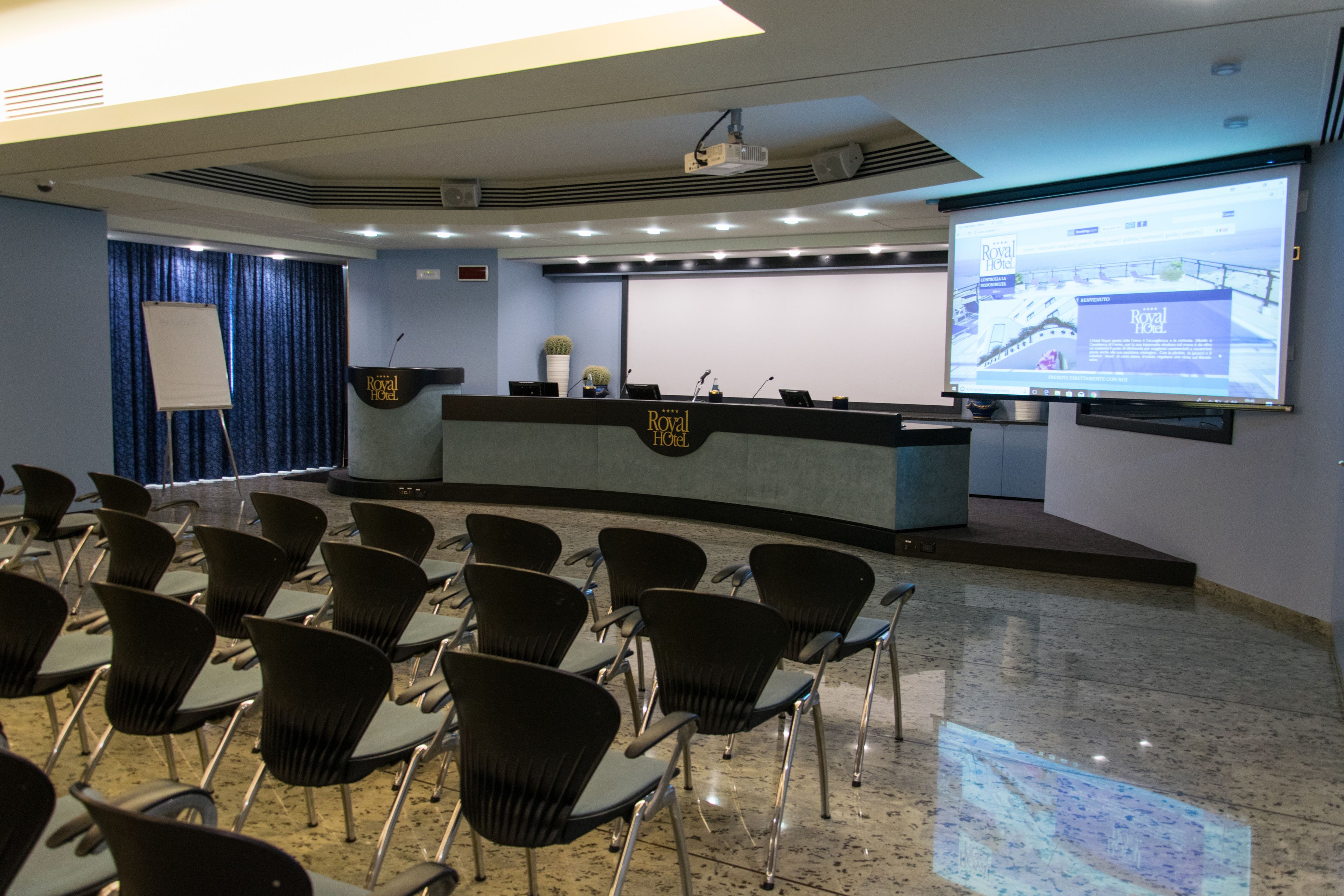 A conference room with a podium, a projection screen, and rows of chairs.