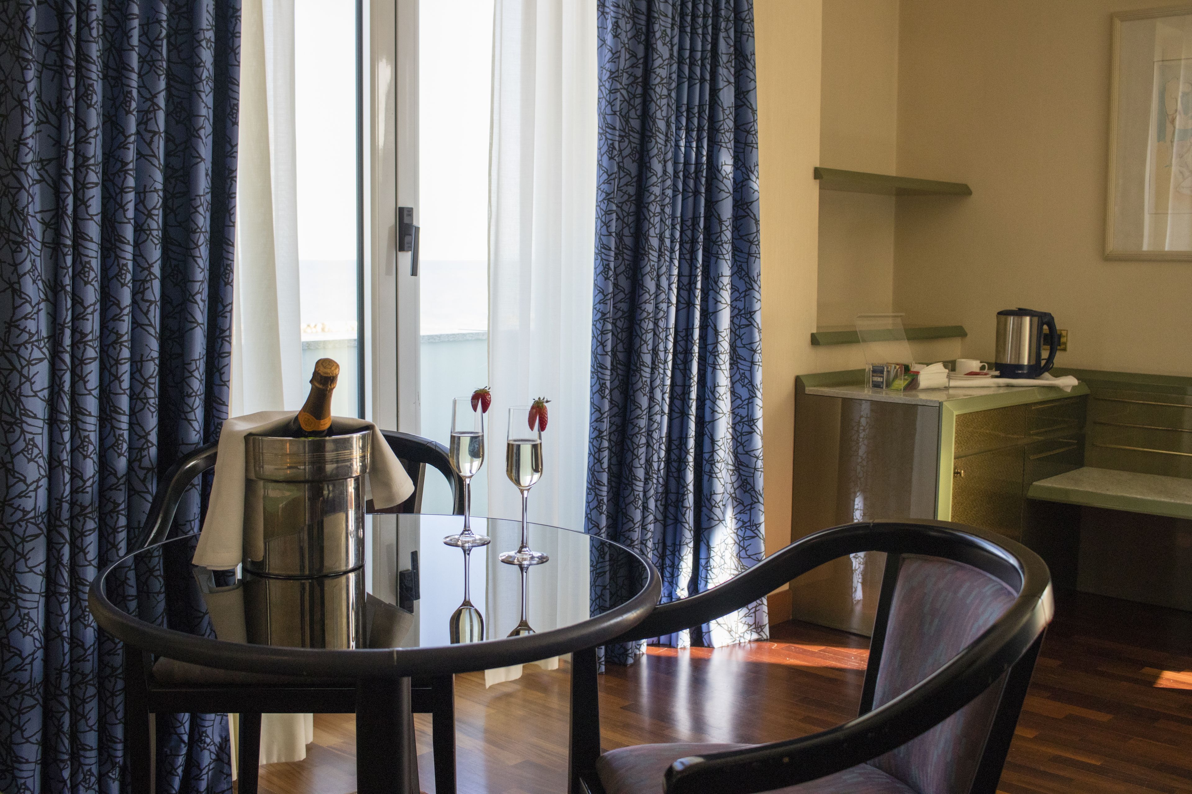 A dining area with a round table, chairs, a coffee maker, and a kitchen area in the background.