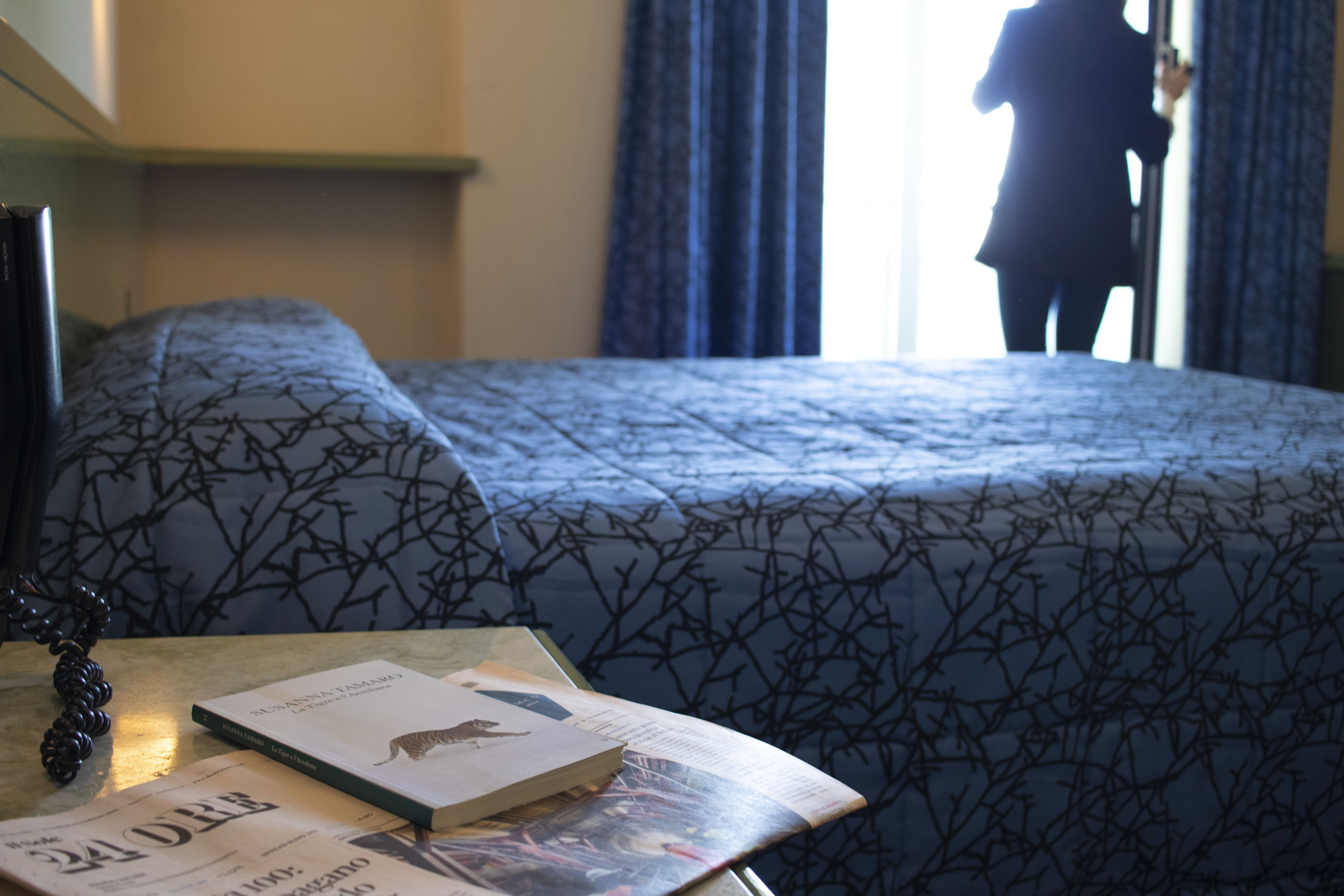 Una camera d'albergo con un letto, un tavolo con dei libri e una finestra con tende.