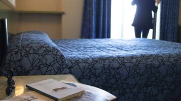Una camera d'albergo con un letto, un tavolo con dei libri e una finestra con tende.