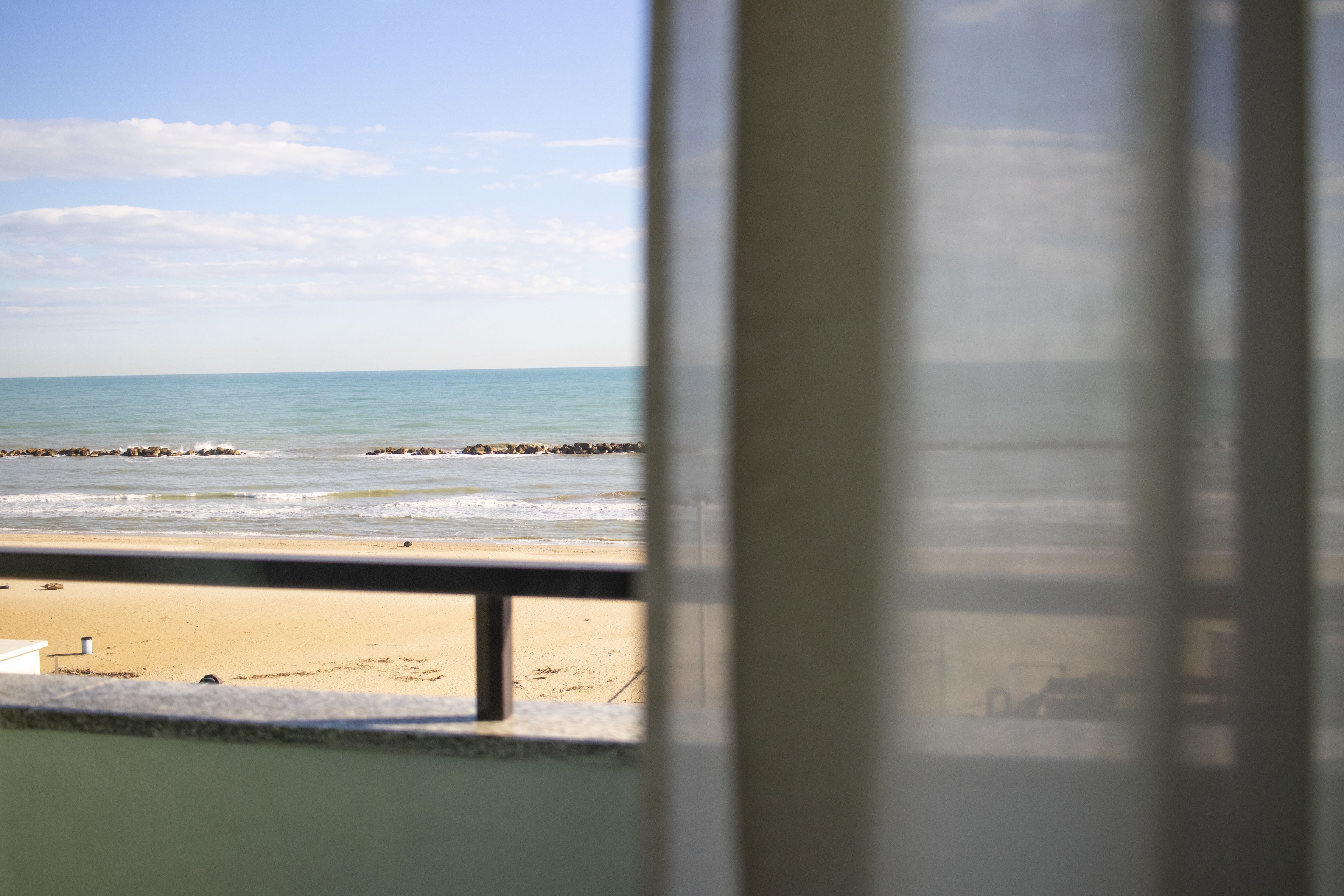 Vista d'una platja a través d'una finestra amb barana metàl·lica.
