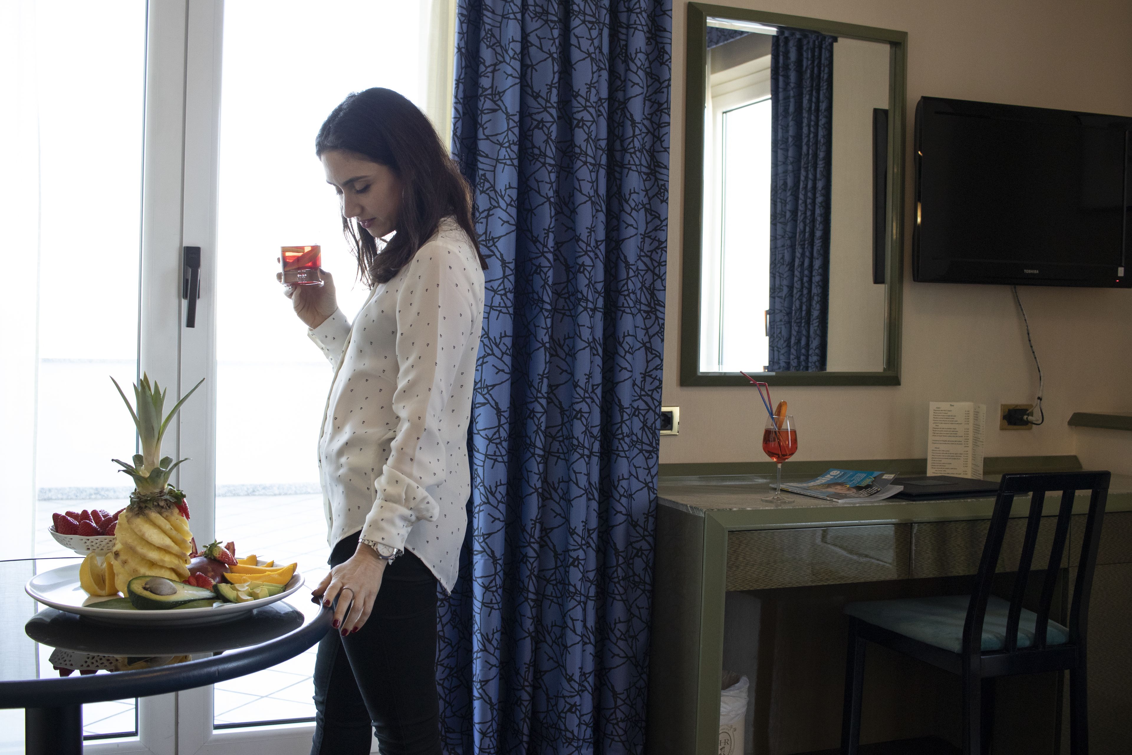 Een hotelkamer met een eettafel, een stoel, een aan de muur bevestigde televisie en een raam met gordijnen.