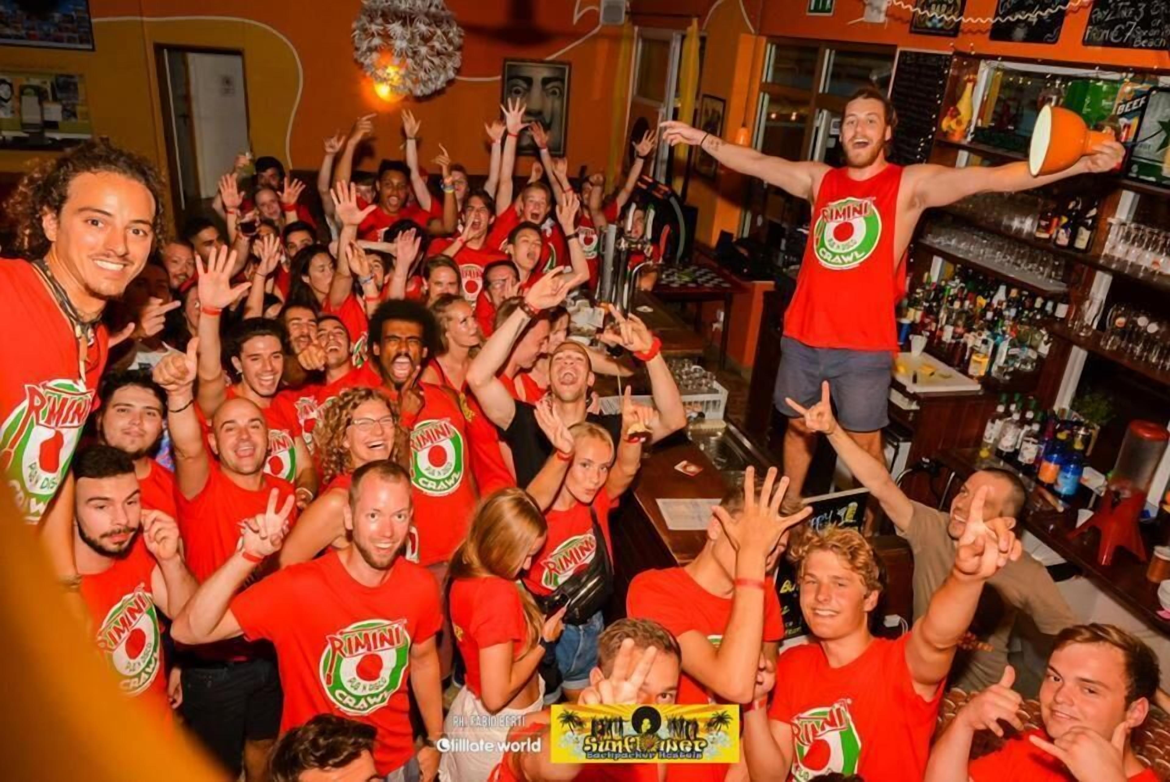 Un bar concurrido, con gente vestida de rojo, un camarero y estantes llenos de botellas.
