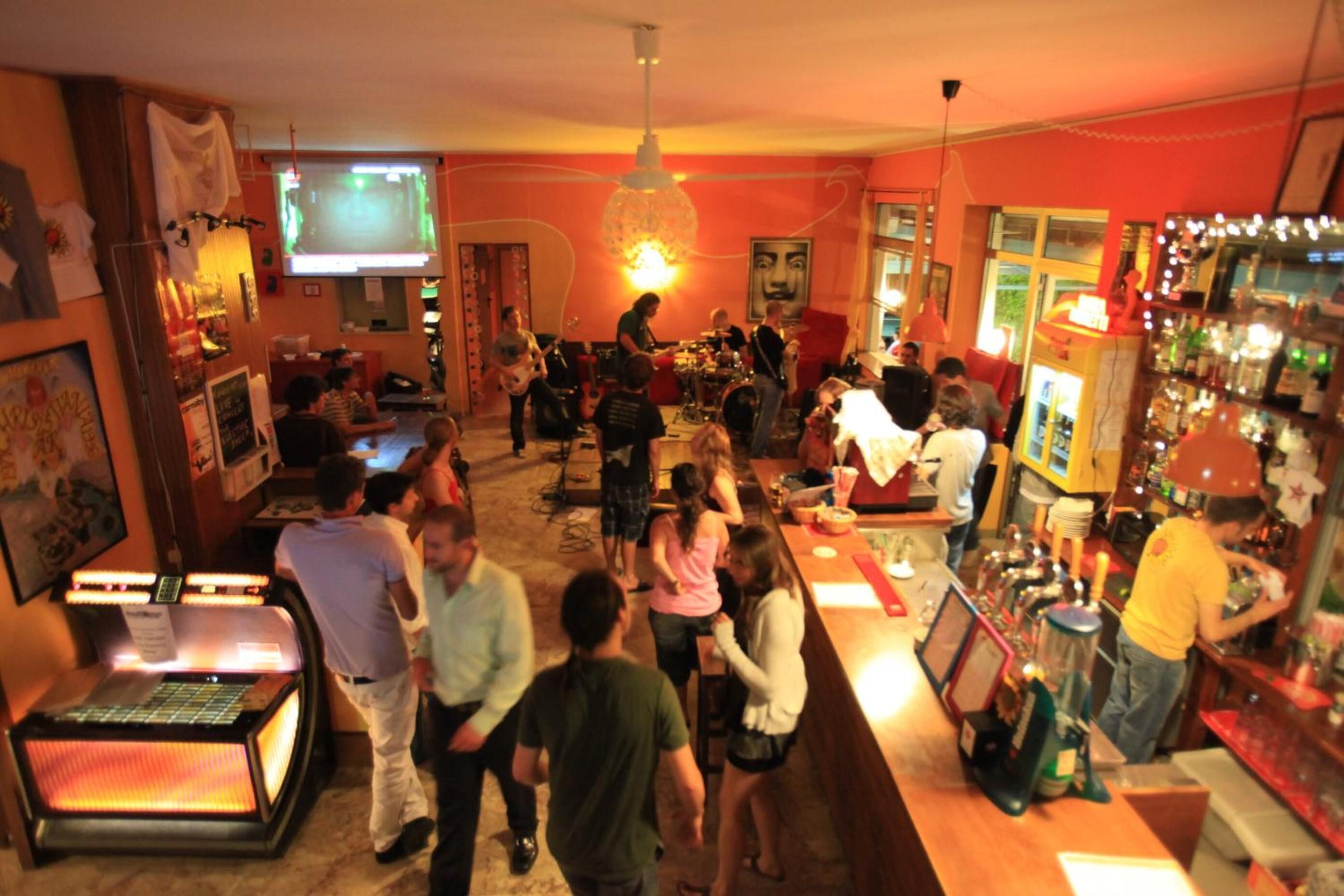 A bar area with a jukebox, a stage for live music, and a bartender.
