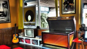 A room with a vintage jukebox, a guitar, a television, and a poster of a musician.