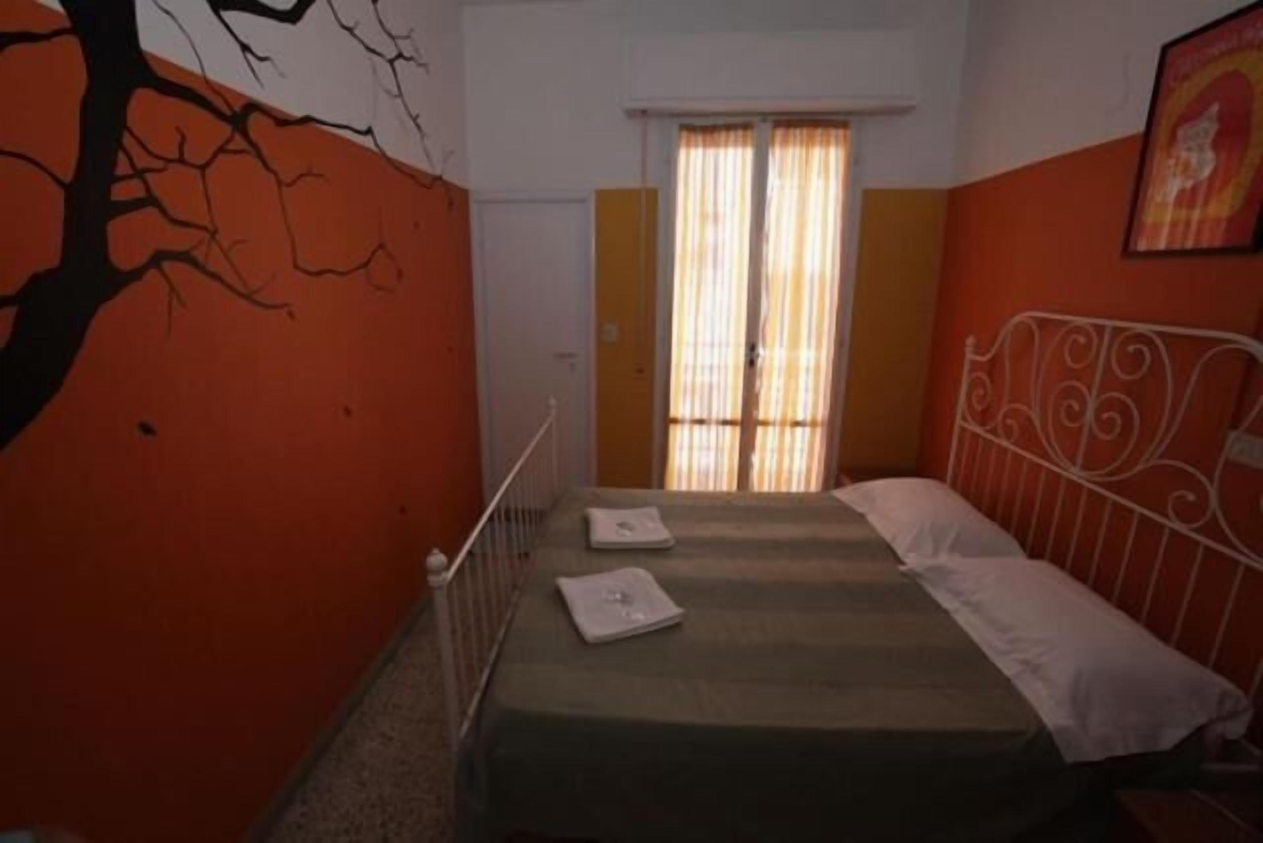 A room with a bed, a window with curtains, and a wall with a tree mural.