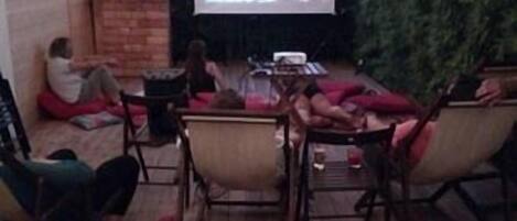 An outdoor patio with wooden flooring, a projector screen, and string lights.