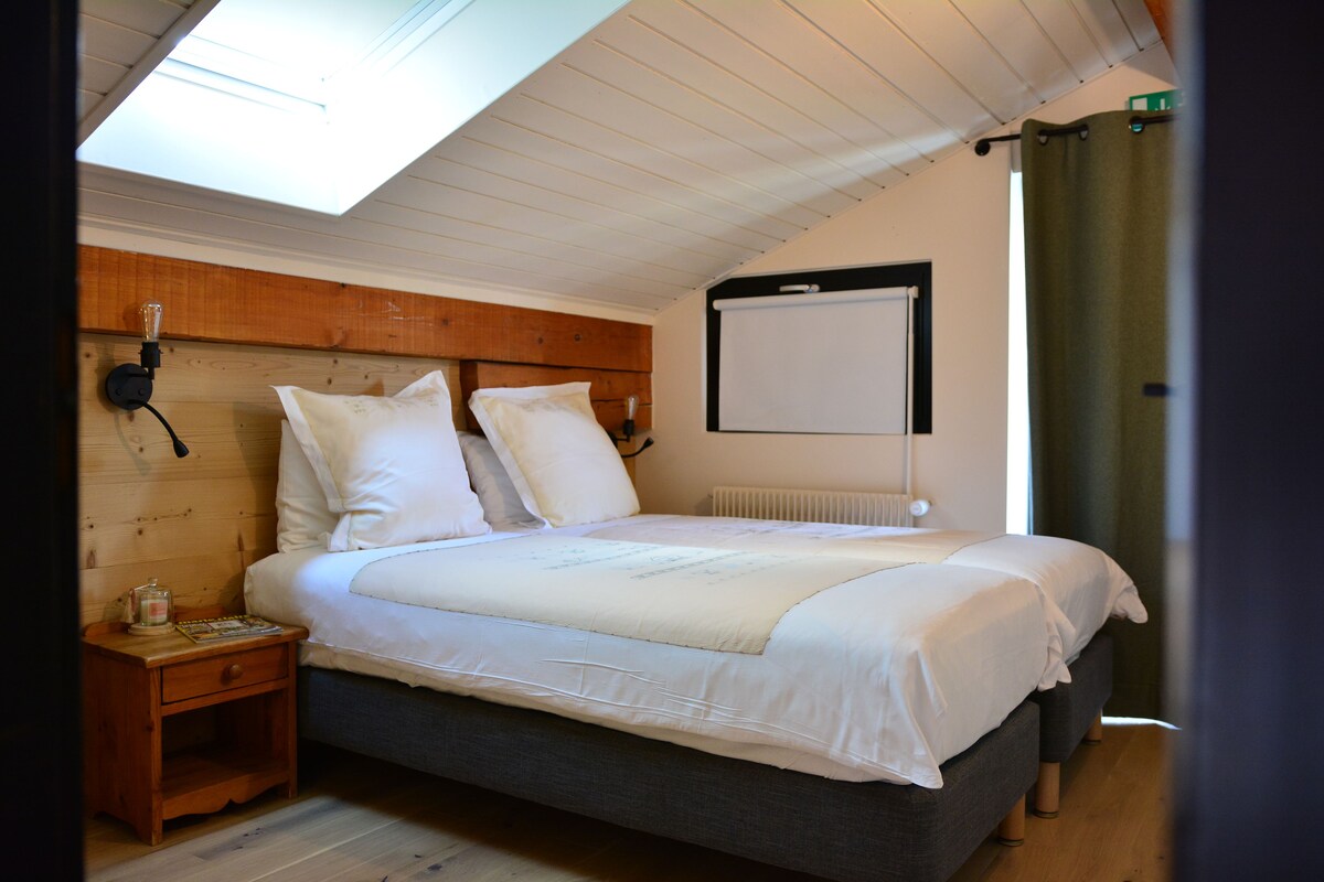 A bedroom with a bed, a nightstand, a wall-mounted projector, and a window with curtains.