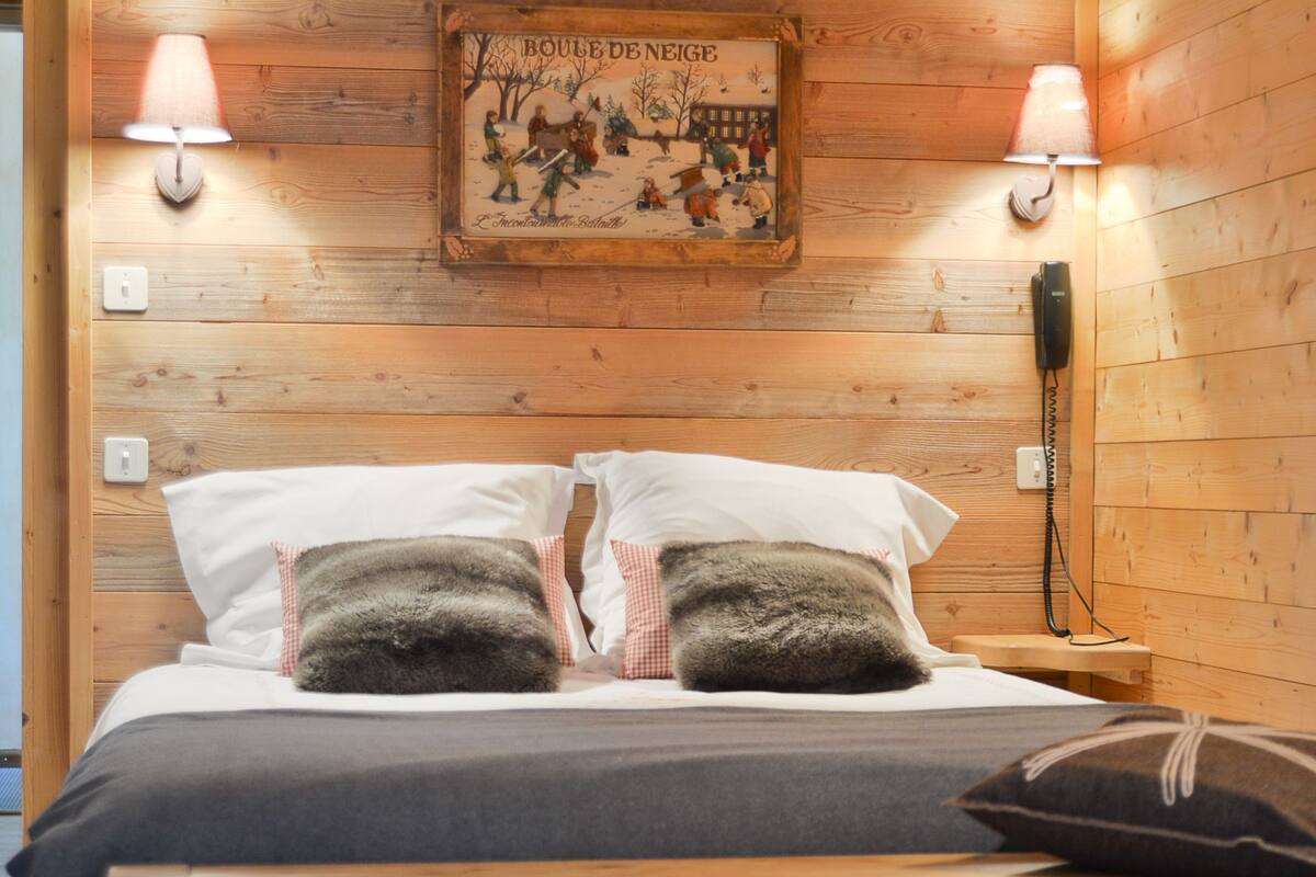 A wooden-paneled bedroom with a bed, two wall-mounted lamps, a telephone, and a framed picture on the wall.