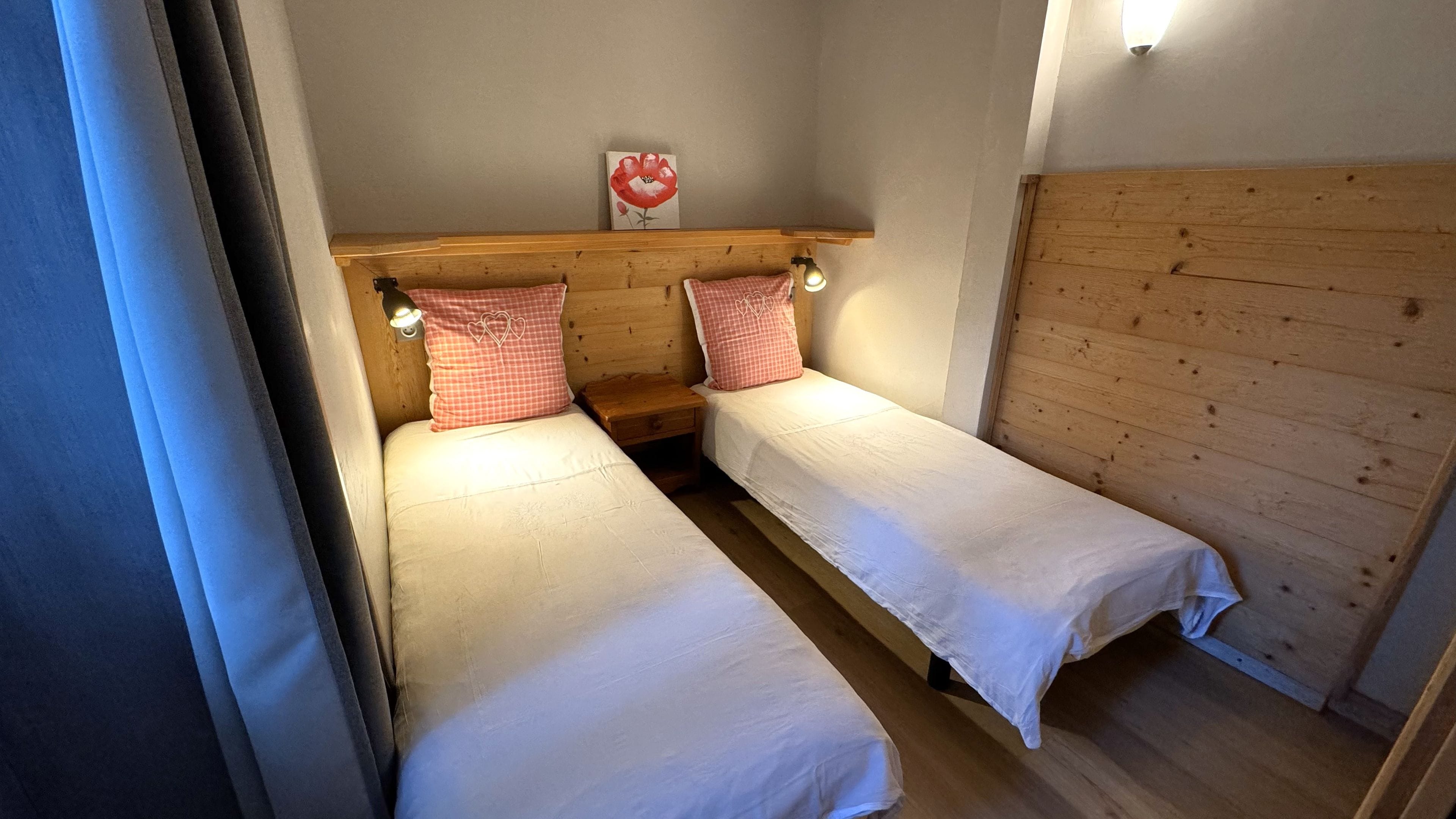 A small, cozy room with two single beds, wooden headboards, and a wall-mounted light fixture.