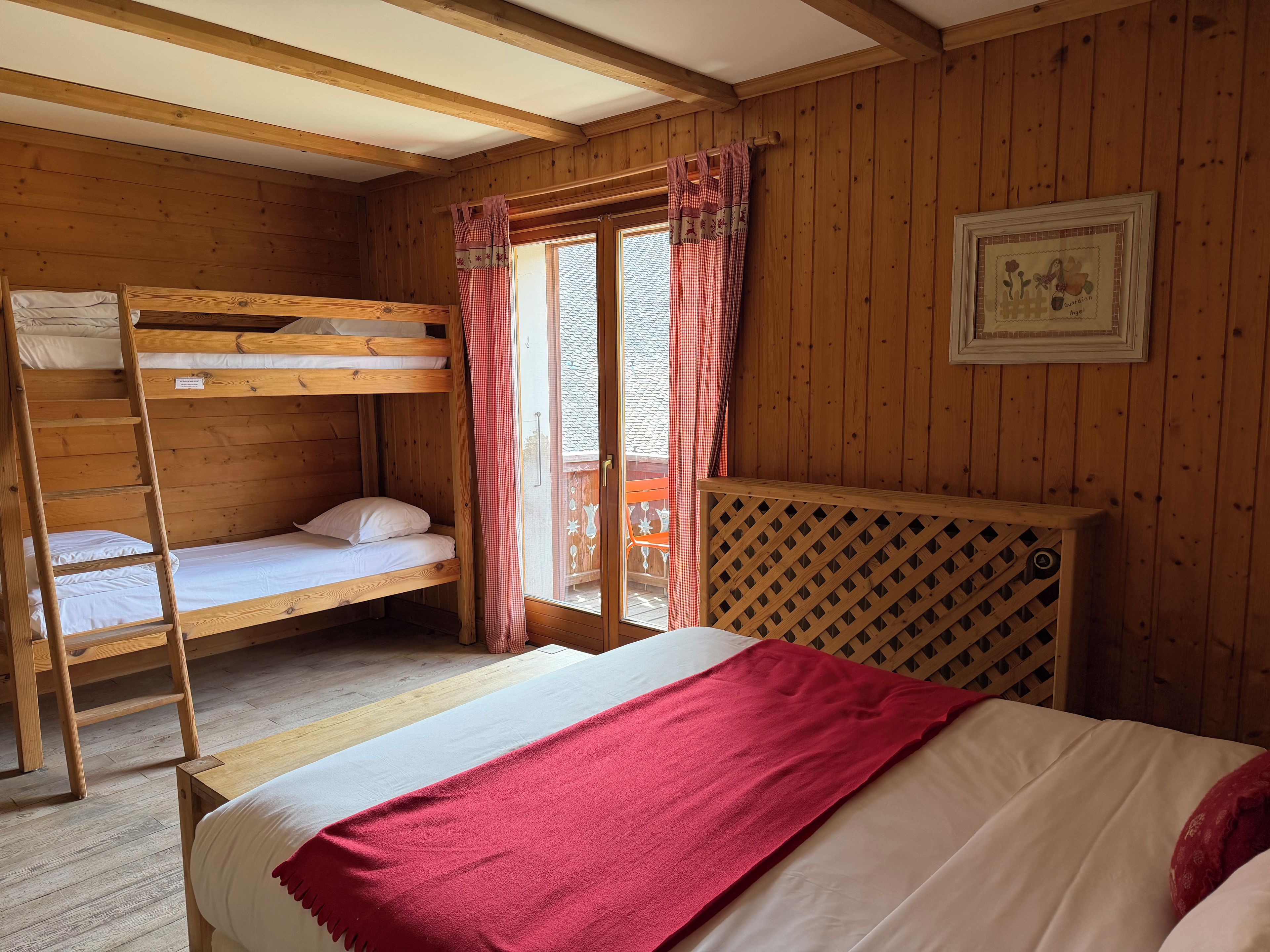 Habitación de cabaña de madera con literas, una escalera, una manta roja y un panel divisor de madera entretejida.