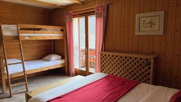 Habitación de cabaña de madera con literas, una escalera, una manta roja y un panel divisor de madera entretejida.
