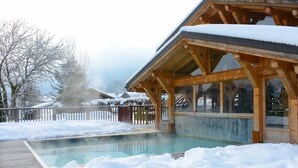Une cabane en bois avec une piscine, le tout entouré de neige.