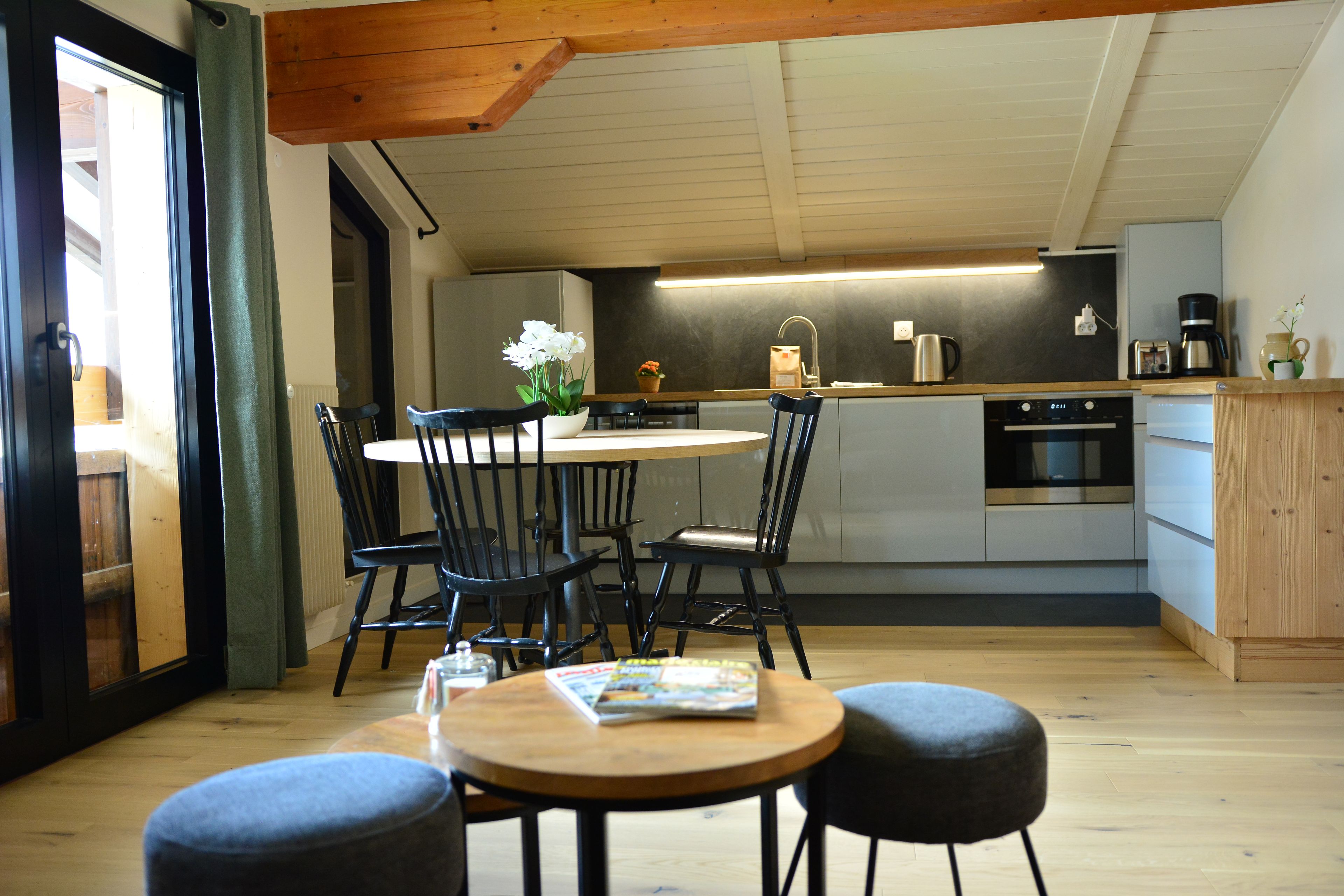 A modern kitchen with a dining area, wooden flooring, and a view of the outdoors.