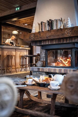 A cozy restaurant interior with a fireplace, wooden bar, and bar stools.. Café-Hôtel Le Morillon