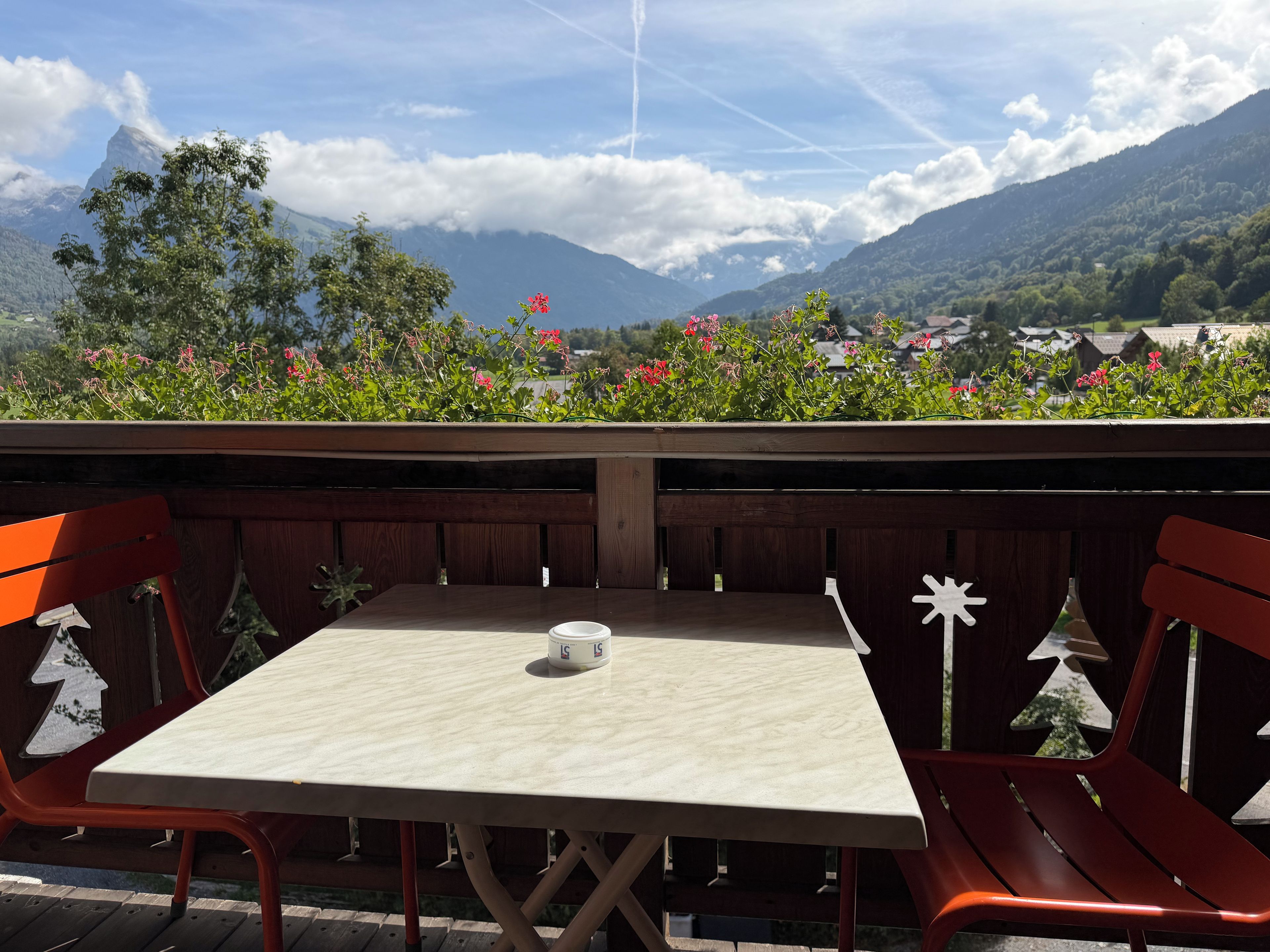 A table with a cup on it, surrounded by red chairs, with a mountain view in the background.