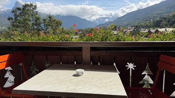 Una mesa con una taza, rodeada de sillas rojas, con vista a la montaña al fondo.