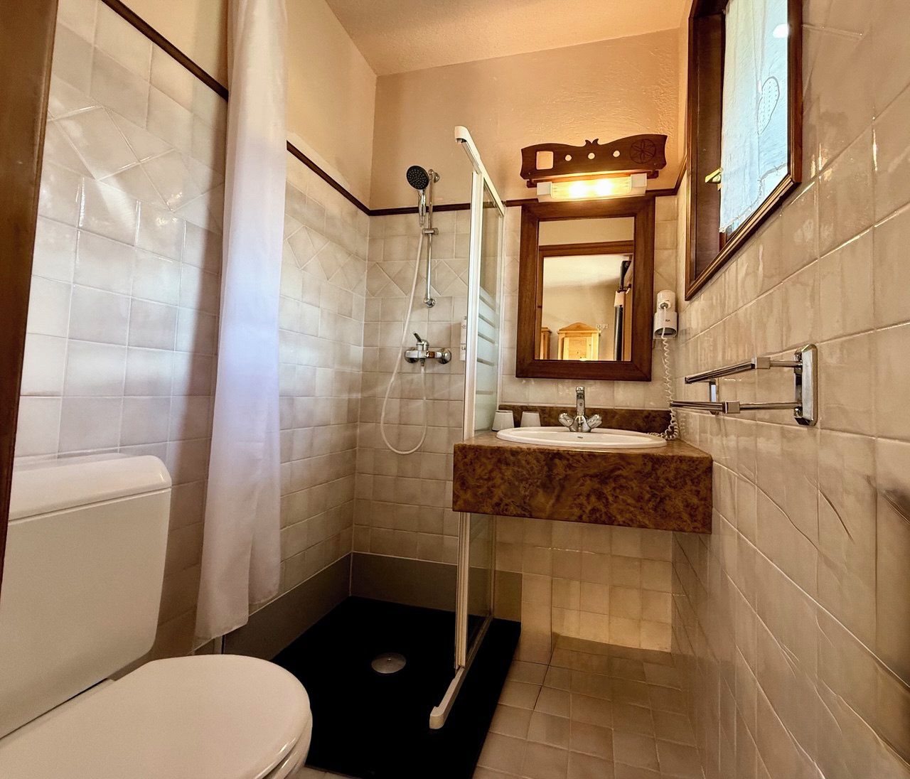 A bathroom with a toilet, a sink with a marble countertop, a shower with a handheld showerhead, and a mirror with a wooden frame.