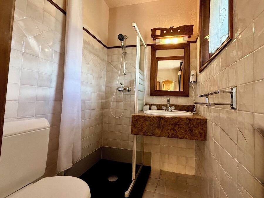 Un baño con inodoro, lavamanos con encimera de mármol, ducha con cabezal de ducha manual y espejo con marco de madera.