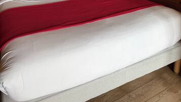 Ein Bett mit weißer Bettwäsche und einer roten Decke, Holzwände und einer Wandleuchte.