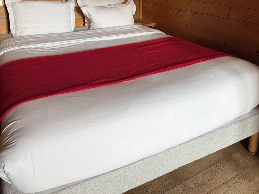 Ein Bett mit weißer Bettwäsche und einer roten Decke, Holzwände und einer Wandleuchte.