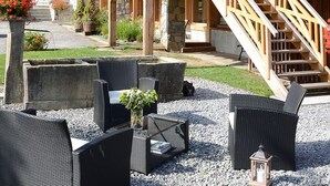 Un chalet en bois doté d’un balcon orné de fleurs rouges, d’un espace salon extérieur et d’un escalier menant à l’étage supérieur.