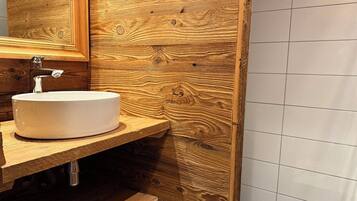 Un baño con tocador de madera, un lavamanos blanco y un espejo.